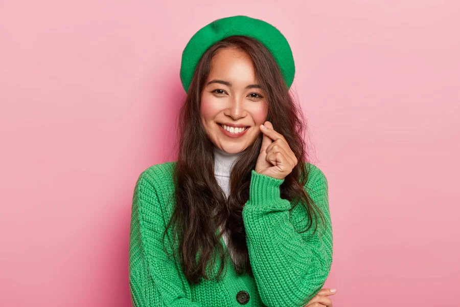 beautiful woman wearing green clothes smiling while being in a pink background setting